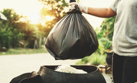 Man holding trash bag over trash bin.